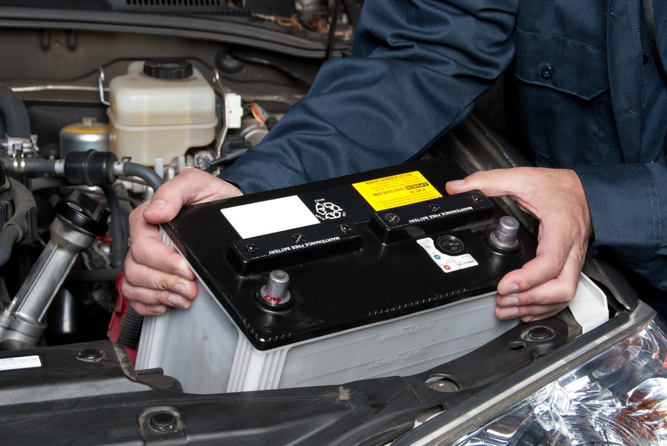 auto technician installing a new car battery into vehicle