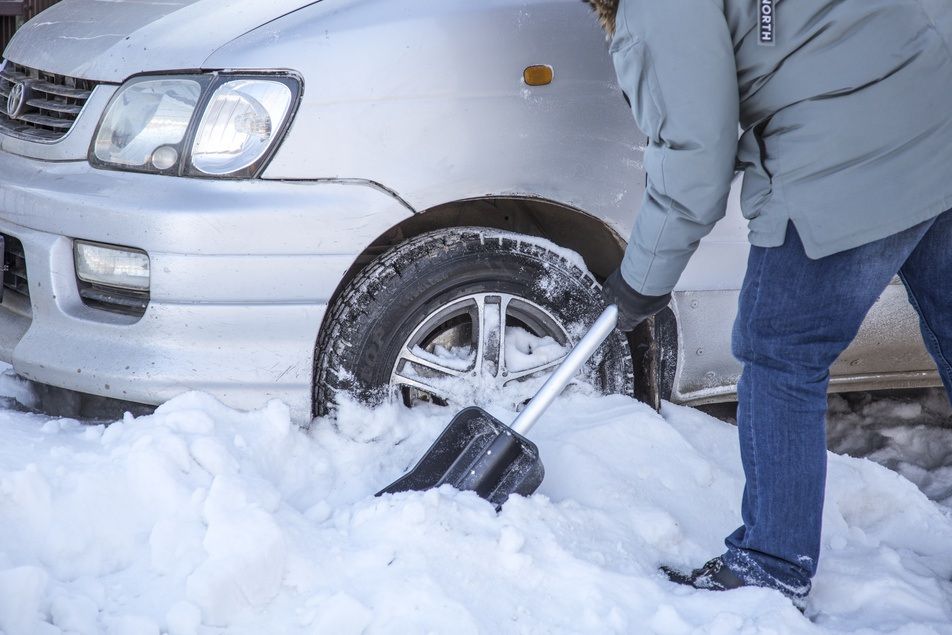 man using snow shovel to dig out car
